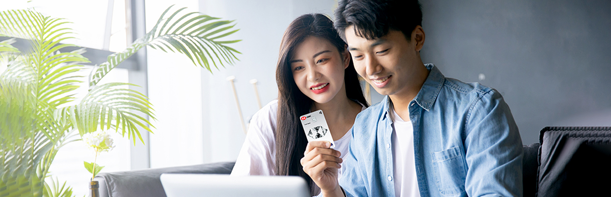 a young couple sitting on a sofa holding a tablet and an HSBC card; image used for HSBC Vietnam understanding your credit card statement article page.