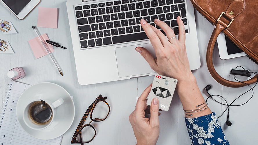 A woman using laptop with another hand holding an HSBC card. 