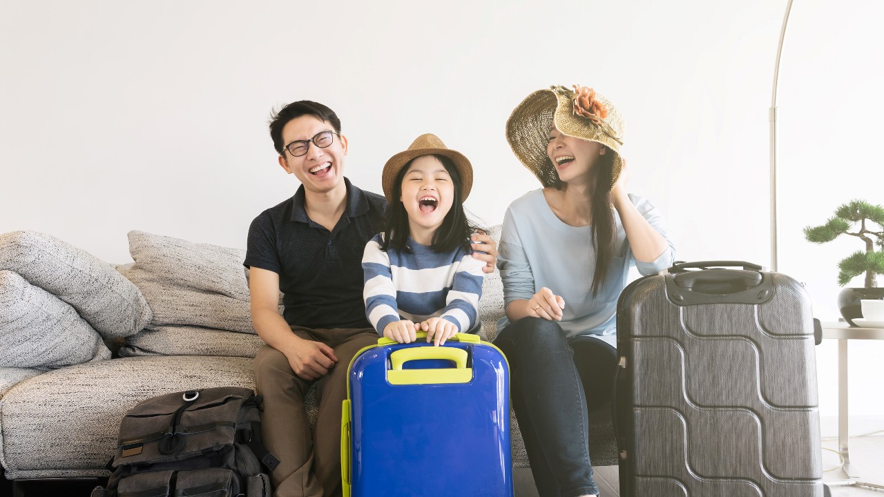Happy family of three sitting with luggage on sofa in living at home; image used for HSBC Vietnam Credit card rewards explained article page