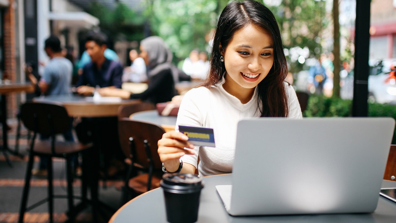 Woman using laptop with a bank card in hand; image used for HSBC Vietnam Debit Card FAQ page