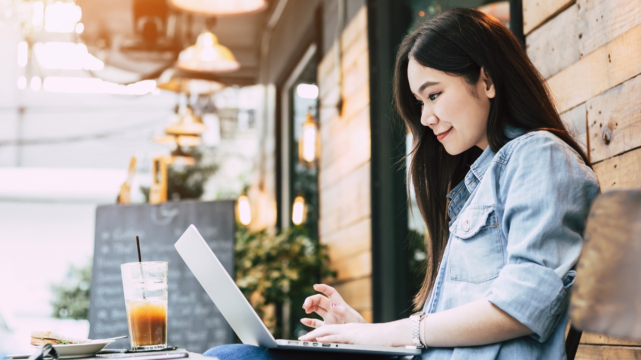A young woman using a laptop on an outdoor table of a coffee shop; image used for HSBC Vietnam Online Savings Account page.