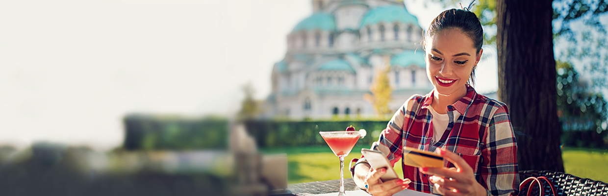 Woman on phone with debit card and cocktail in a park; image used for HSBC Vietnam Debit Card Privilege Club page