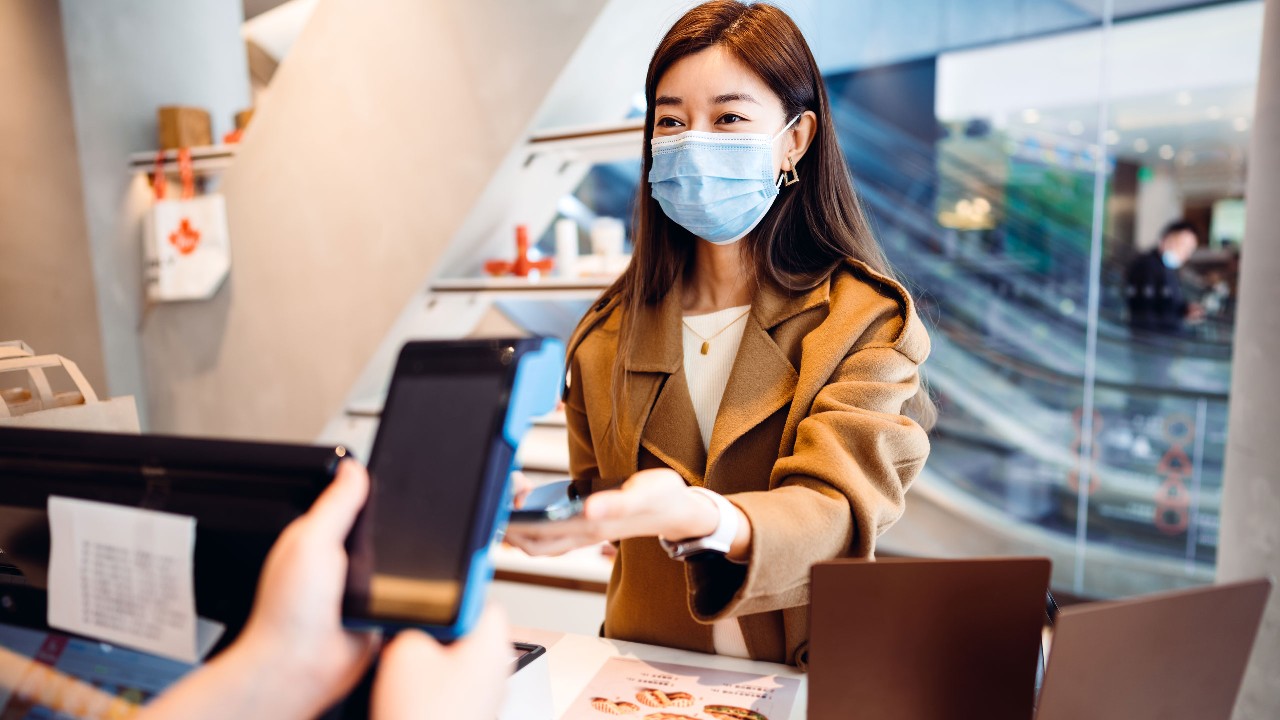 A woman is standing at the check out and using Samsung Pay on the phone to pay her purchase