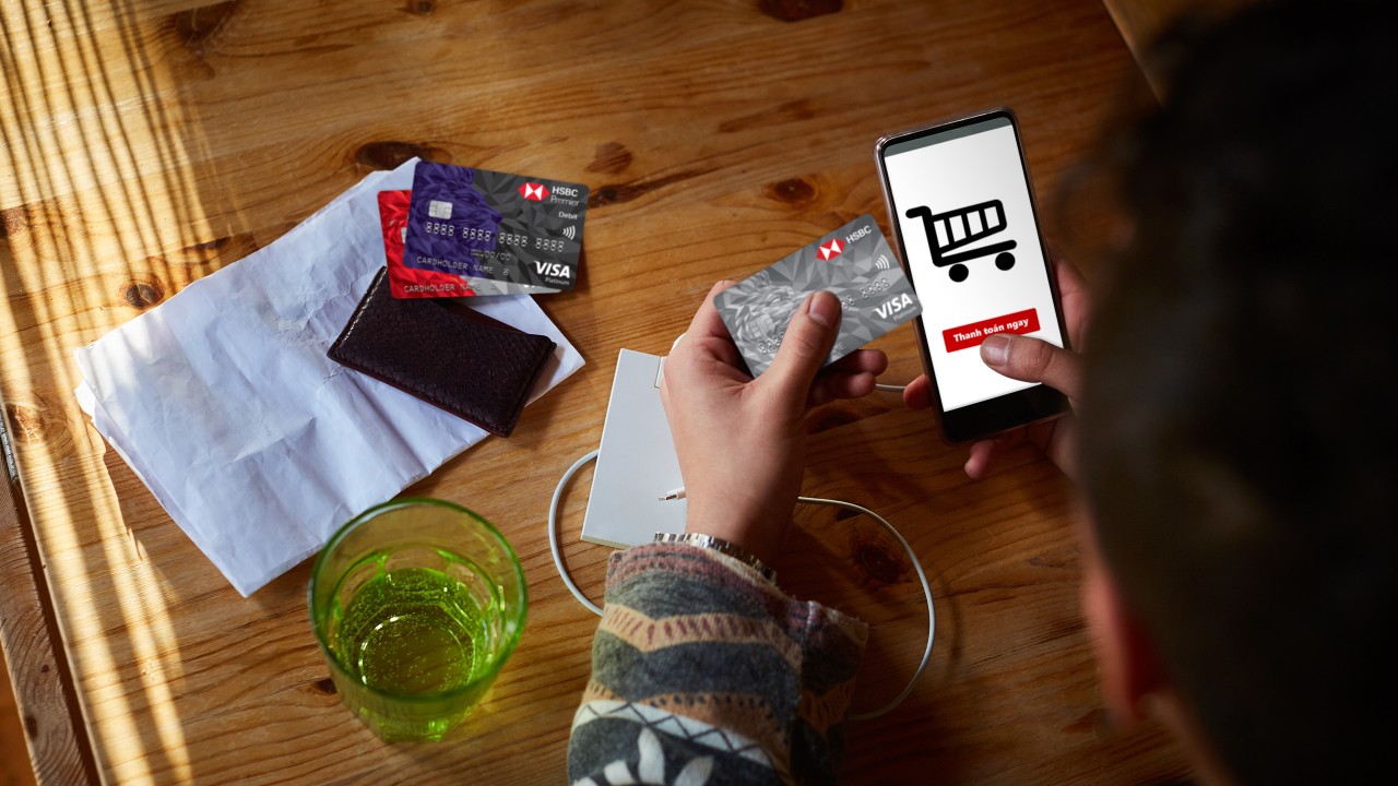 một chàng trai đang cầm thẻ HSBC và sử dụng điện thoại để mua sắm thanh toán online