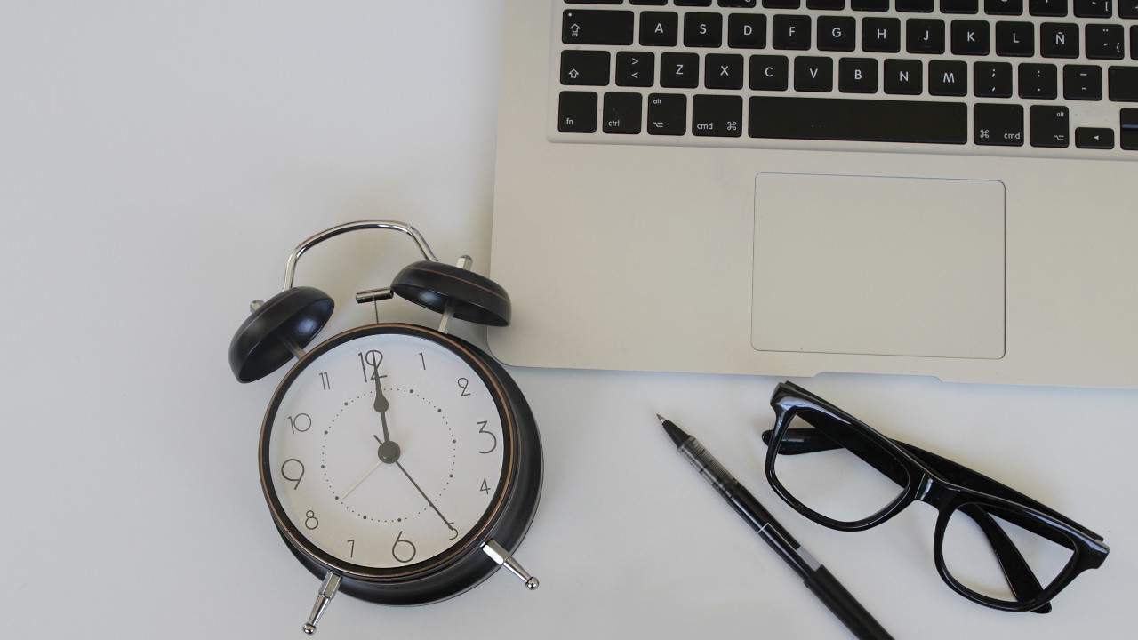 A table set with a laptop, a pair of glasses, an alarm clock, a pen and a notepad; image used for HSBC Vietnam Annual Fee waiver page. 