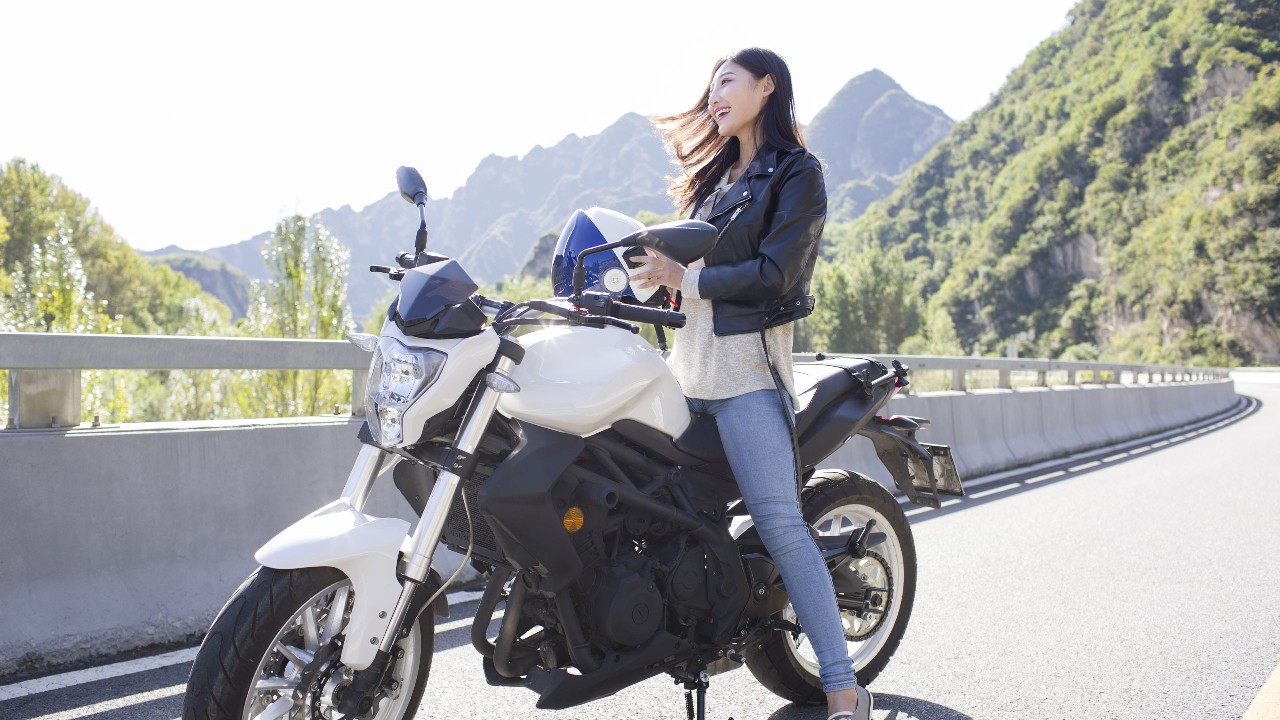 a young woman is sitting on a motor cycle and holding the helmet