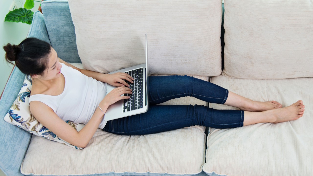 a woman lying on a sofa, using her laptop
