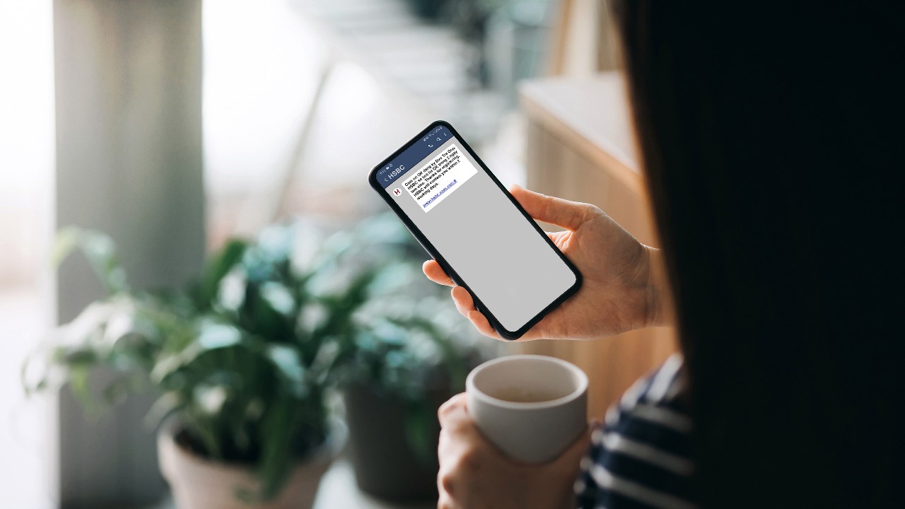 a woman holding a cup and mobile phone with the screen showing a notification from HSBC