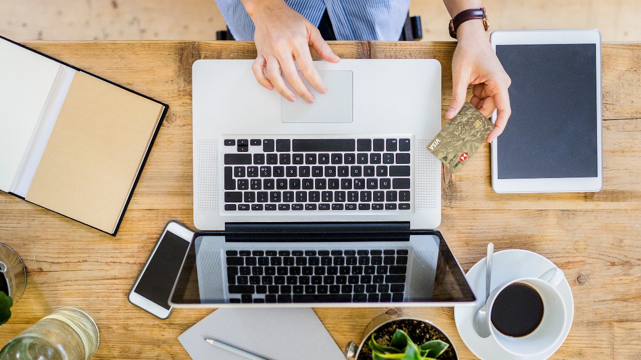 A woman using laptop with another hand holding an HSBC card.