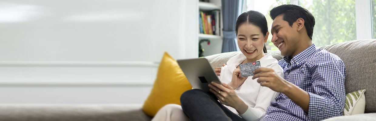 a young couple sitting on a sofa holding a tablet and an HSBC card; image used for HSBC Vietnam understanding your credit card statement article page.