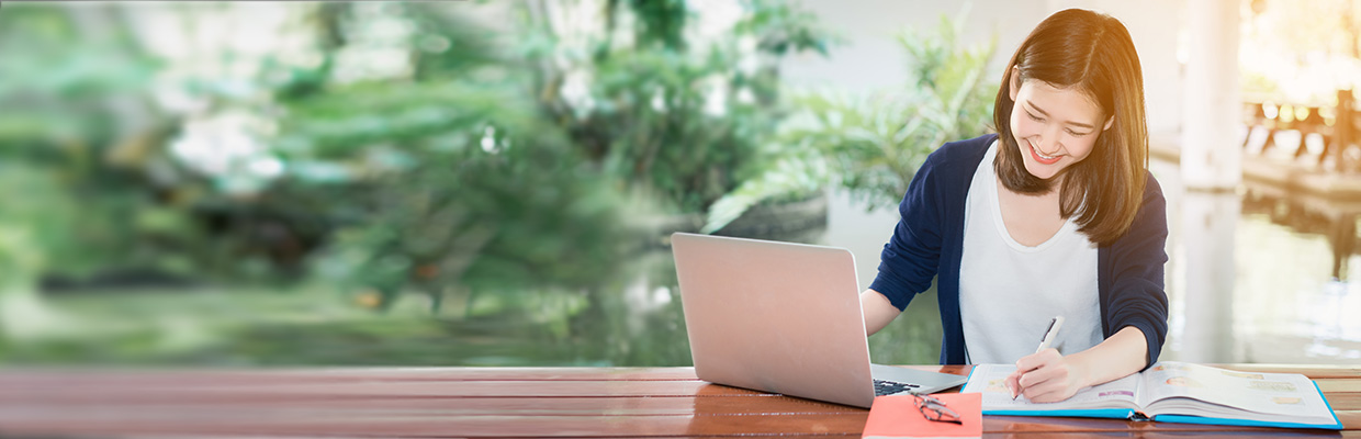 A woman writing in notebook with a laptop aside; image used for how to avoid credit card fees article page.