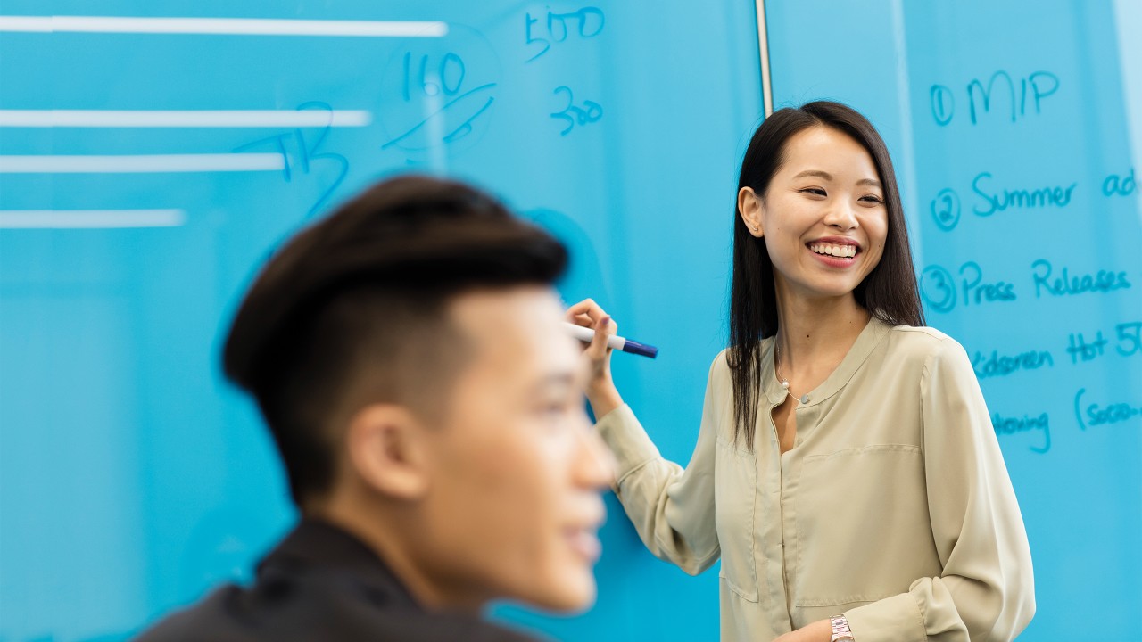 A woman is smiling while writing on a board and a man’s head in front is blurry because of near to the camera; image used for HSBC Vietnam debit card privilege club page