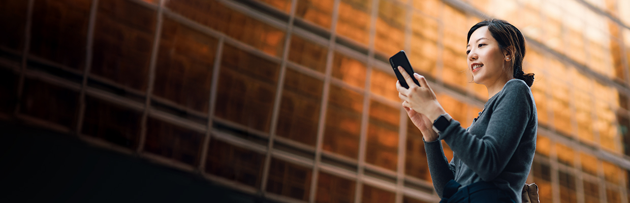 A female using mobile phone outside ; image used for HSBC Vietnam Mobile Banking page